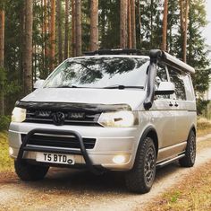 a silver van parked on the side of a dirt road in front of some trees