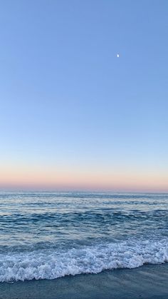 the ocean waves come in to shore as the moon is rising over the horizon and there are no clouds