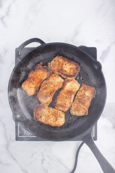 four pieces of meat cooking in a frying pan