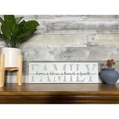 a wooden sign sitting on top of a table next to a vase and potted plant