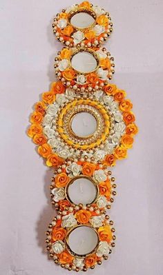 an orange and white wall hanging with three candles on top of each other, surrounded by flowers