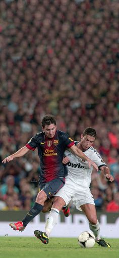 two men are playing soccer in front of an audience at a sporting event, one is trying to kick the ball