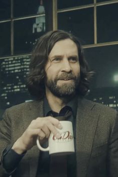 a man with long hair is holding a coffee mug in front of a cityscape