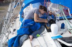 a woman sitting on top of a sailboat working on the side of her boat