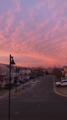 the sky is pink and purple as the sun goes down in this residential area with cars parked on the street