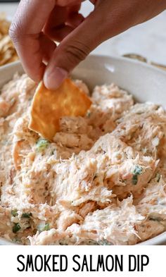 a hand dipping a cracker into a bowl of smoked salmon dip