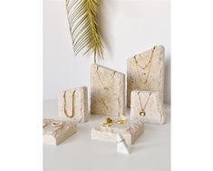 four pieces of white marble with gold necklaces and rings on them next to a palm tree