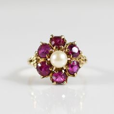 This exquisite ring features a delicate flower design crafted from lustrous 10k yellow gold, showcasing a captivating central pearl surrounded by vibrant synthetic rubies. The contrast between the creamy pearl and the rich, fiery red rubies creates a striking visual appeal. Elegant and timeless, this ring is perfect for adding a touch of sophistication to any ensemble. Size: 5 Metal Type: 10K Yellow Gold (Tested) Weight: 3.7G Width: 14.99mm to 1.62mm at shank Finger to Top of Ring: 8.49mm Hallmarks: 10K SA Center Stone Details:  Type: Pearl Dimensions:5-5.5mm Accent Stones: Type: Synthetic Ruby Quantity: 6 Dimensions:4mm We look forward to providing you with an exceptional experience and helping you find more exquisite additions to your collection. *More Pictures Available on Request* Ruby Flower, Pearl Cluster, Vintage Pearl, Anniversary Ideas, Fiery Red, Vintage Pearls, Ruby Ring, Delicate Flower, Pink Wedding