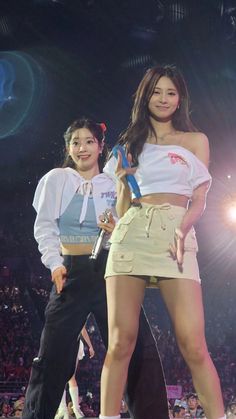 two women standing on stage with one holding a microphone and the other wearing short shorts