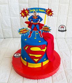 a superman birthday cake on a table with white tile wall behind it and red plate holding the cake