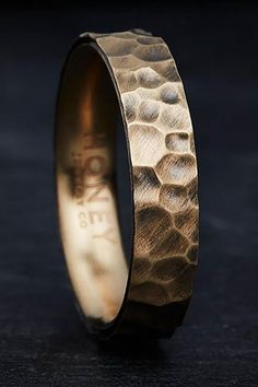 a gold wedding ring with an etched design on the outside and inside, sitting on a black surface