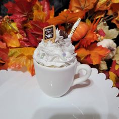 a white cup filled with whipped cream sitting on top of a table next to fall leaves