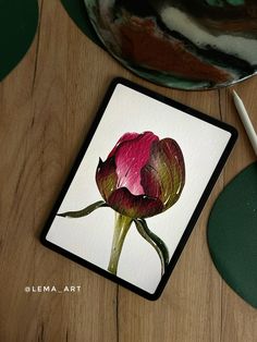 a painting of a pink flower on a white card next to a pen and paper