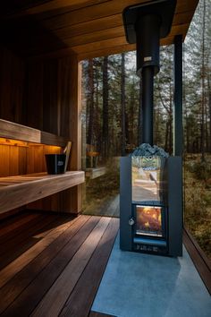 a wood burning stove sitting on top of a wooden floor next to a bench and trees