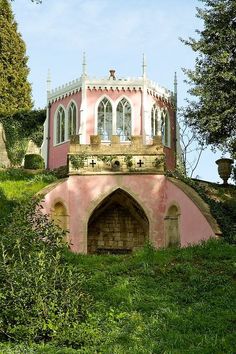 a pink and white building sitting on top of a lush green hillside next to trees