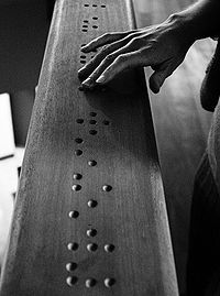 black and white photograph of a person's hand on a long wooden bench with holes in it