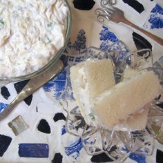 a bowl of cream cheese next to a sandwich on a glass plate with spoons