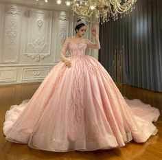 a woman in a pink ball gown standing on a wooden floor next to a chandelier