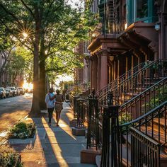 people walking down the sidewalk in front of some buildings with trees on both sides and stairs leading up to them