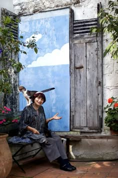 a woman sitting on a bench in front of a door with a cat standing on top of her head