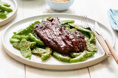 steak and green beans on a white plate with two bowls of seasoning in the background