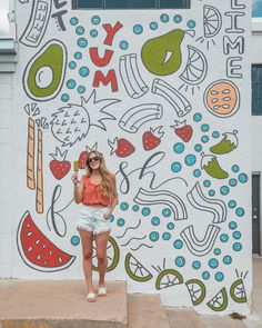 a woman standing in front of a wall painted with colorful doodles and fruit on it