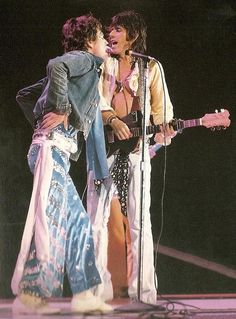 two people standing next to each other while one person is holding a guitar and singing