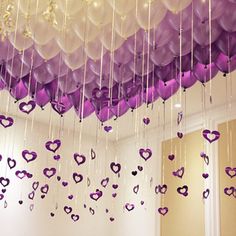 purple and white balloons hanging from the ceiling with hearts attached to them in a room