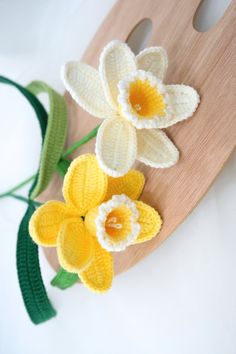 two crocheted daffodils sitting on top of a wooden cutting board