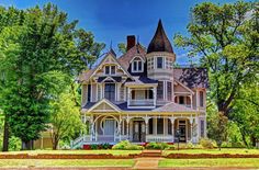 an old victorian style house in the middle of a park with lots of trees and bushes