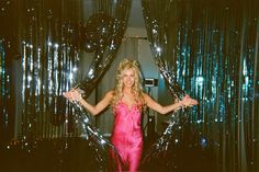 a woman in a pink dress posing for a photo with shiny balloons behind her and the backdrop is blue