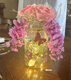 a glass jar filled with pink flowers on top of a wooden table covered in fairy lights