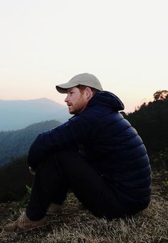 a man sitting on top of a grass covered hillside