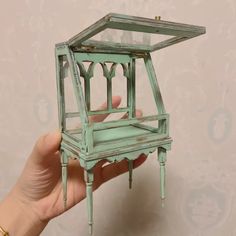 a hand holding a miniature green birdcage in it's left side,