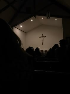 people are sitting in pews at a church with a cross on the wall behind them