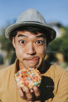 a man wearing a hat and holding a doughnut with sprinkles on it