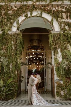 a bride and groom kissing in front of an entrance to a building with greenery