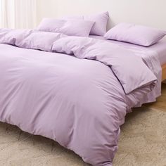 a bed with purple sheets and pillows in a room