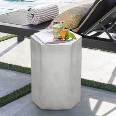 an outdoor table with magazines and drinks on it next to a swimming pool in the background