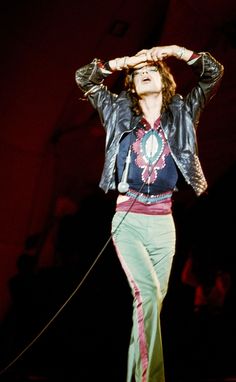 a man with long hair standing on stage holding his hands up to his head while wearing a leather jacket