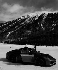 a black and white photo of a car in the snow with mountains in the background