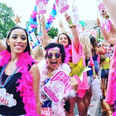 two women in pink and black outfits are holding up signs while others walk down the street