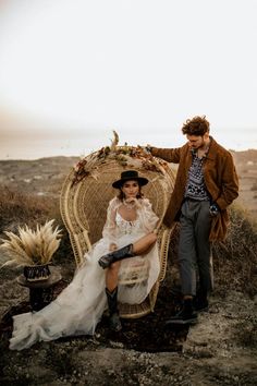 a man standing next to a woman in a white dress sitting on a wicker chair