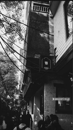 black and white photograph of people walking on the sidewalk in front of a building with awnings