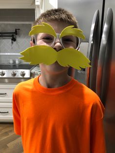 a young boy with fake mustaches on his face in front of a refrigerator freezer