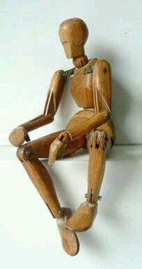 a wooden mannequin sitting on the ground with its legs crossed and head turned to the side