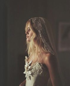 a woman in a wedding dress with a veil on her head and hair down, looking off to the side