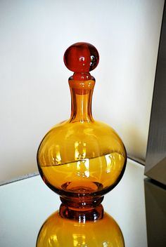 a yellow glass vase sitting on top of a table next to a white wall and floor