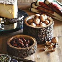 nuts and cheese are in wooden bowls on a table next to other food items, including bread