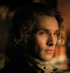 a close up of a person wearing a suit and tie with long curly hair, looking at the camera